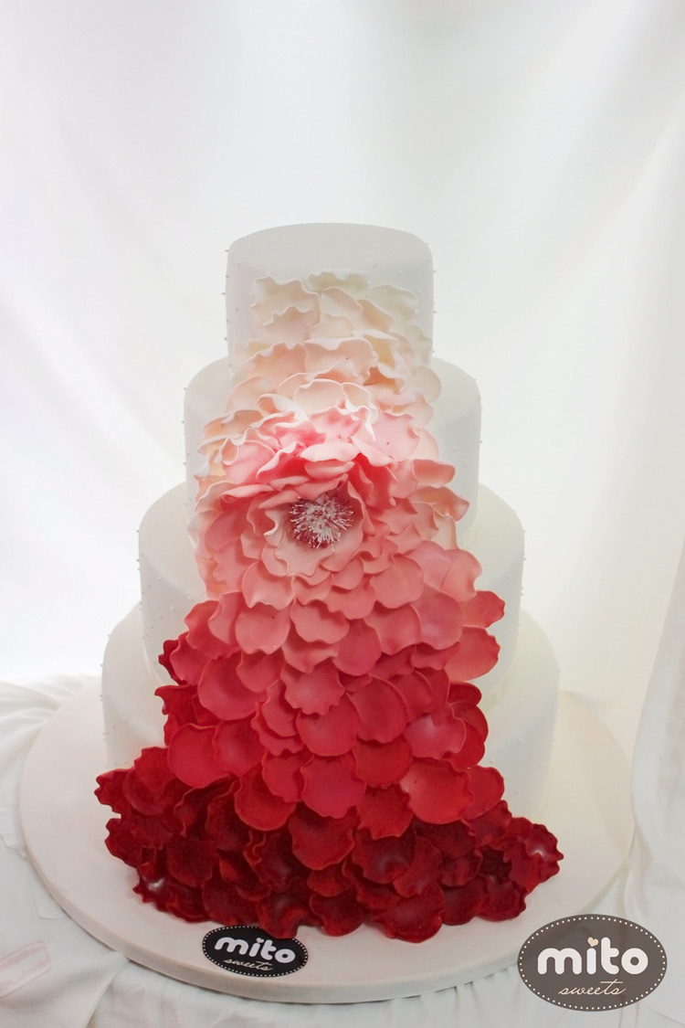 Chiếc bánh cưới trở nên nổi bật hơn, hấp dẫn hơn nhờ những bông hoa trang trí màu hồng đỏ thắm.
