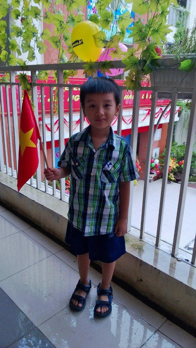 Bé Anh Kiên cầm cờ chờ đợi ngày khai giảng tại trường Mầm non Quỳnh Mai.
