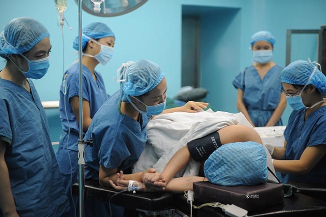 Guo Jia được yêu cầu nằm nghiêng, co người, hai tay nắm lấy nhau đề duỗi nhằm tạo tư thế chuẩn trong khi tiêm gây tê màng cứng. 
