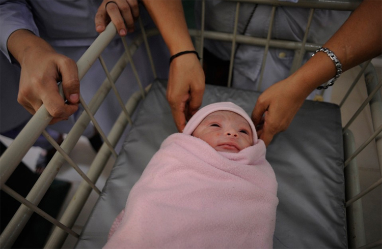 Em bé được đưa về phòng mẹ trong chiếc xe đẩy bởi các y tá.
