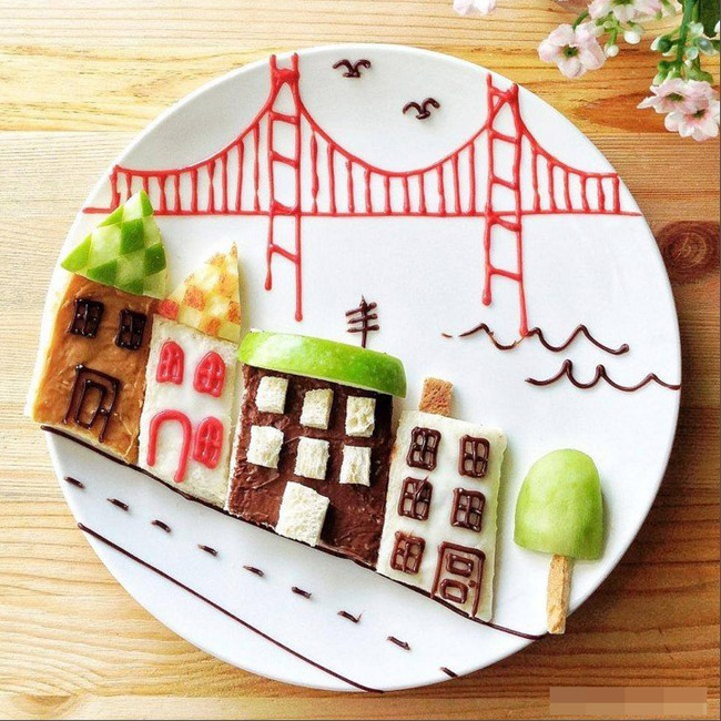 Một thành phố bằng bánh ngọt, táo xanh, sô cô la cùng cây cầu vô cùng đơn giản cũng là một ý tưởng hay để các mẹ trang trí món ăn cho bé.
