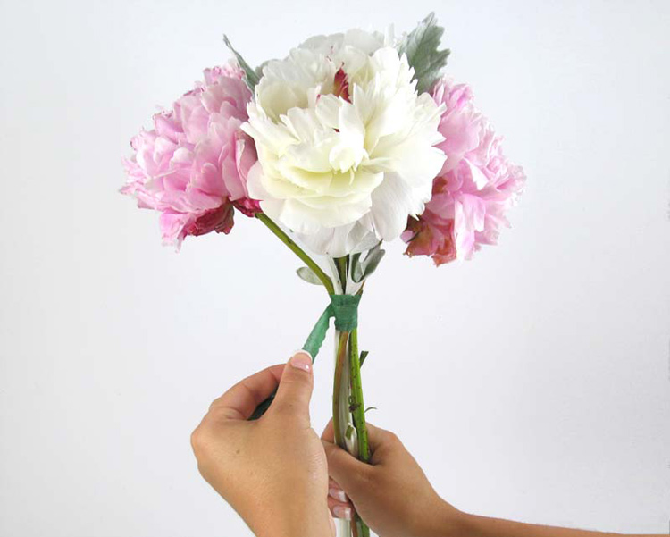 Tiếp theo, xếp thêm 2 cành hoa nữa, để màu sắc so le nhau. Dùng băng dính cuốn nhiều vòng sát phần cuống hoa để tạo hình cho bó hoa.
