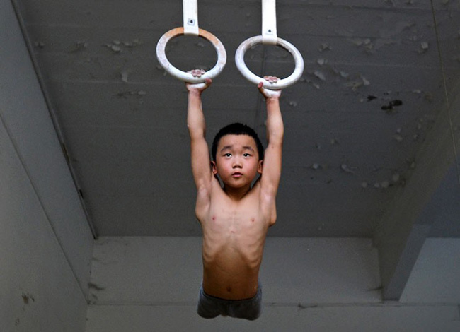 Một cậu bé trong đội thể dục dụng cụ, đang thực hiện các động tác trên cao.
