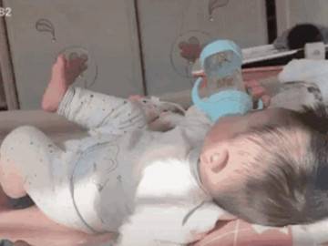 Bé trai có thú vui tao nhã, vừa uống sữa vừa xoay chân đốn tim mẹ bỉm sữa