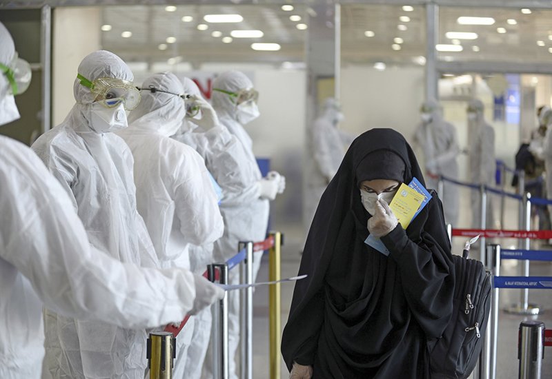 Nhân viên y tế mặc đồ bảo hộ đứng phát tờ hướng dẫn thông tin về dịch bệnh tại sân bay quốc tế Al Najaf, Iraq.
