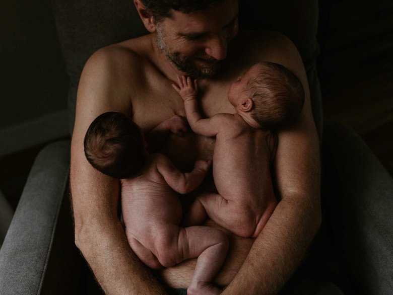 Ông bố hạnh phúc ôm các con của mình trong vòng tay khi đang da kề da. Một em bé cũng dùng cánh tay non nớt bám vào ngực bố đầy âu yếm.