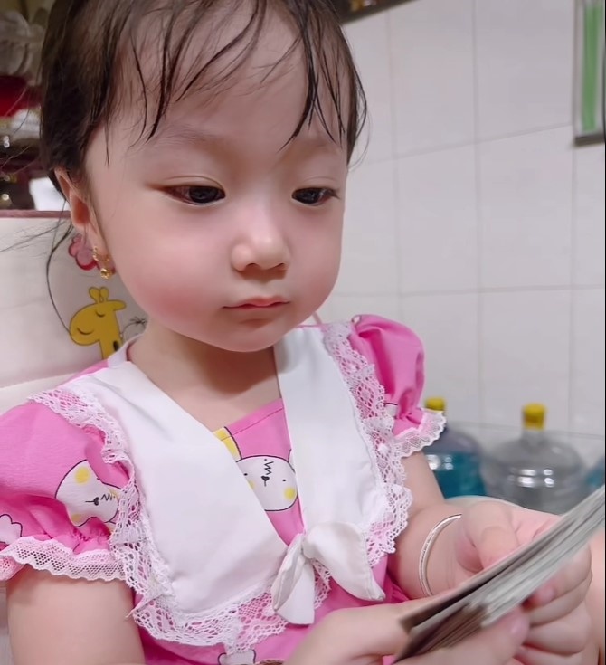 Cô bé cầm sấp giấy hình đồ chơi giả bộ chào mời bán vé số.