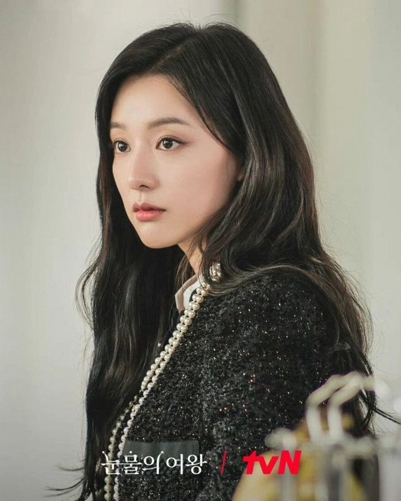 Kim Ji Won diện áo khoác vài tweet màu đen của Chanel phối với áo sơ mi trắng, đeo thêm chiếc vòng cổ ngọc trai dài, toát lên khí chất thanh lịch của một người phụ nữ giàu có.