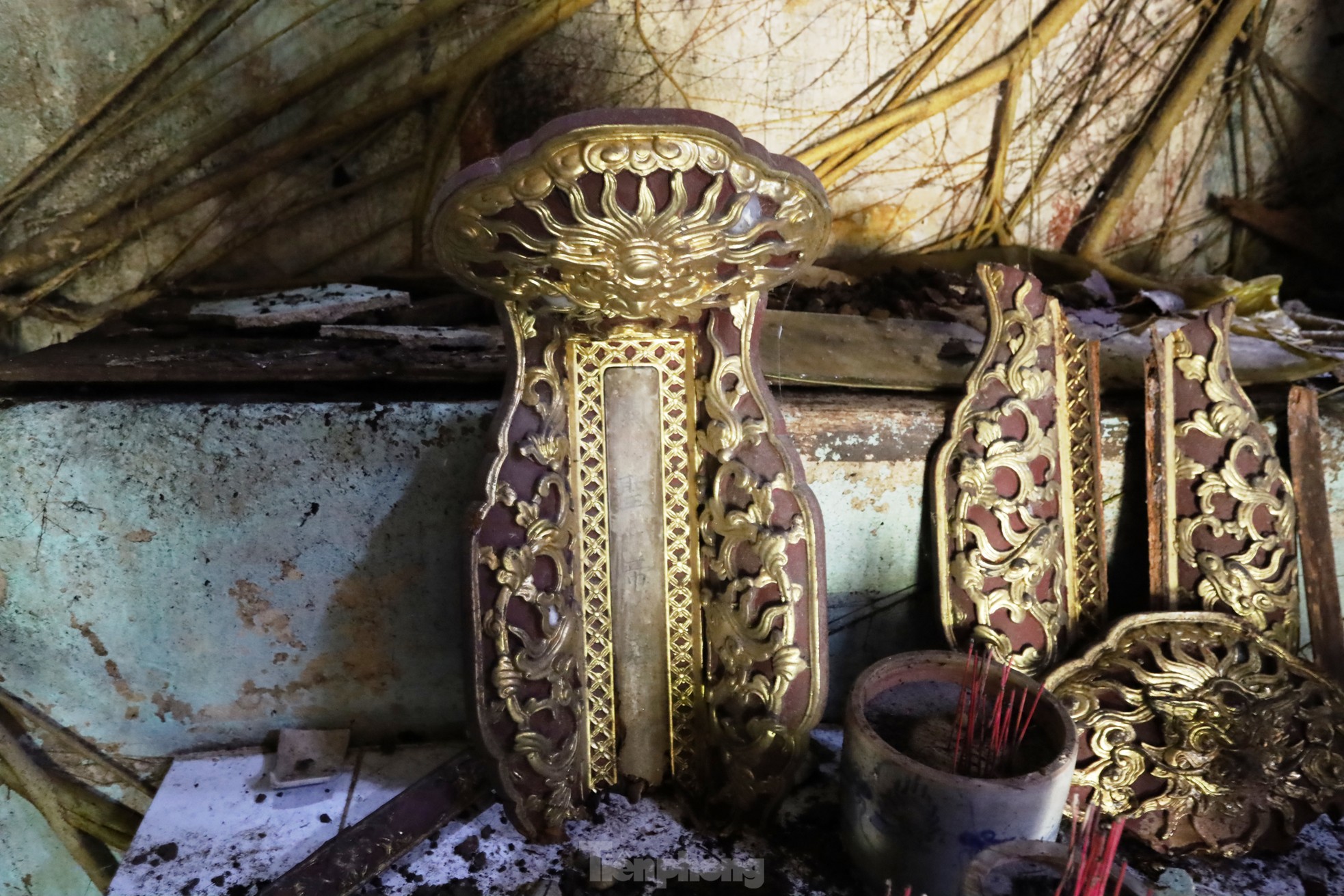 Những mảnh gỗ sơn son thếp vàng, vốn là những phần trang trí tinh xảo của bàn thờ, nay rơi rụng, nứt vỡ, nằm ngổn ngang như chứng tích của một thời huy hoàng đã xa. Chúng từng là biểu tượng của sự tôn nghiêm, gắn với những nghi lễ thiêng liêng xưa, nhưng giờ đây chỉ còn là những tàn dư lặng lẽ, phủ lấp bụi thời gian.