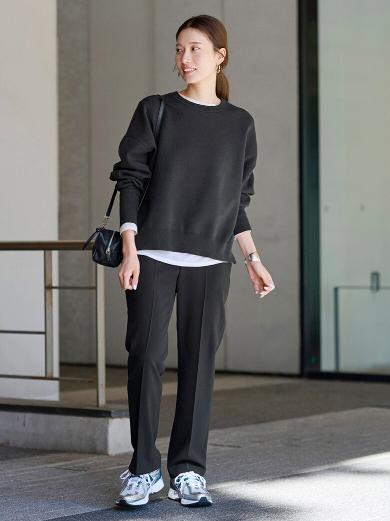 Một chiếc sweater đen oversized được kết hợp cùng áo thun trắng layer bên trong, tạo hiệu ứng layering nhẹ nhàng. Quần tây đen dáng suông mang đến vẻ thanh lịch nhưng không hề cứng nhắc, giúp cân bằng giữa phong cách công sở và trang phục thường ngày.