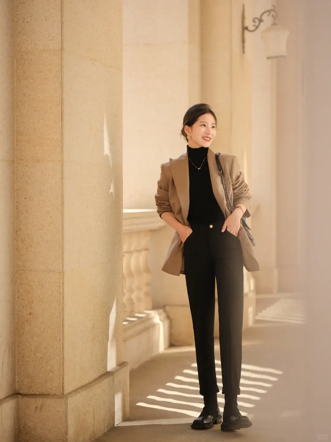 Bộ trang phục mang đậm tinh thần minimalist với sự kết hợp giữa blazer nâu nhạt, áo len cổ lọ đen và quần tây đen ống côn thanh lịch.