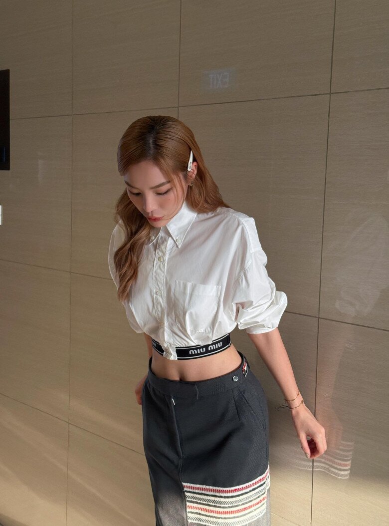 Áo sơ mi trắng croptop kết hợp cùng chân váy midi mang phong cách thể thao hiện đại. Chi tiết cạp váy in logo thương hiệu Miu Miu tạo điểm nhấn tinh tế.