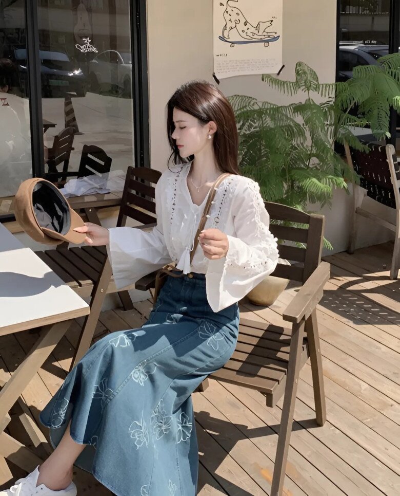 Phong cách vintage pha lẫn bohemian được thể hiện trọn vẹn qua sự kết hợp giữa áo blouse trắng thêu ren tinh xảo và chân váy denim xanh họa tiết thêu hoa đầy nghệ thuật.