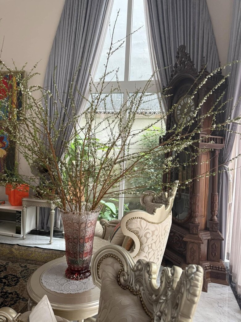 Một góc khác của phòng khách với đồng hồ gỗ chạm khắc cầu kỳ, tạo điểm nhấn cổ điển. Bình hoa cắm trong lọ thủy tinh đỏ đặt trên bàn nhỏ, giúp không gian thêm phần ấm cúng và sang trọng.