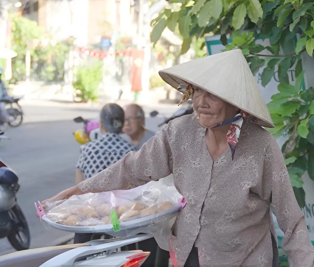 Bà mang bánh đi dọc phố mời mọi người mua giúp