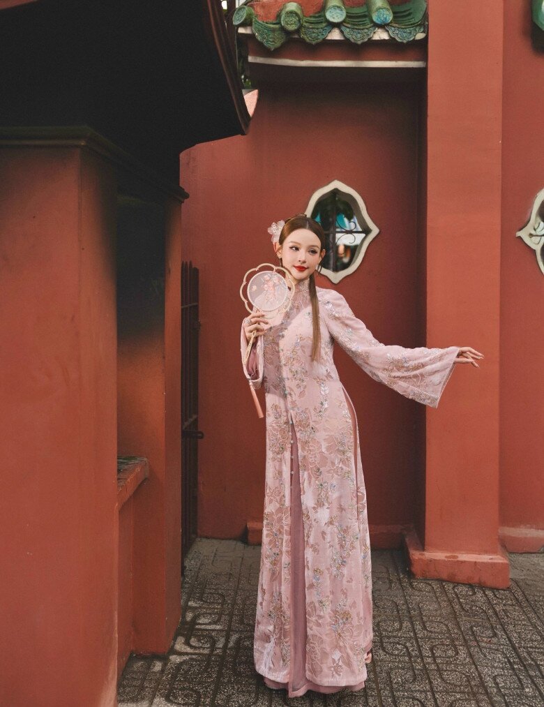 Khoác lên mình thiết kế áo dài ren hồng phấn đính kết hoa nổi 3D tinh xảo, chị đẹp Huyền Baby như bước ra từ bức tranh xuân cổ điển. Tay áo loe nhẹ tạo độ bay bổng, kết hợp phụ kiện quạt tròn cầm tay càng tăng thêm chất Á Đông thanh tao.