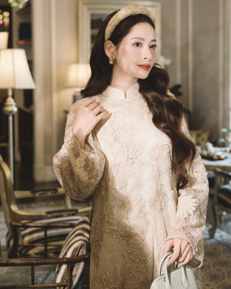 Chi Pu trông như tiểu thư quý tộc với chiếc áo dài ren màu kem gợi nhắc vẻ đẹp quý phái của những buổi tiệc trà cổ điển. Chất liệu ren nổi phủ kín thân áo tạo chiều sâu thị giác, trong khi phom dáng đứng, cổ cao giúp tôn trọn khí chất nền nã.
