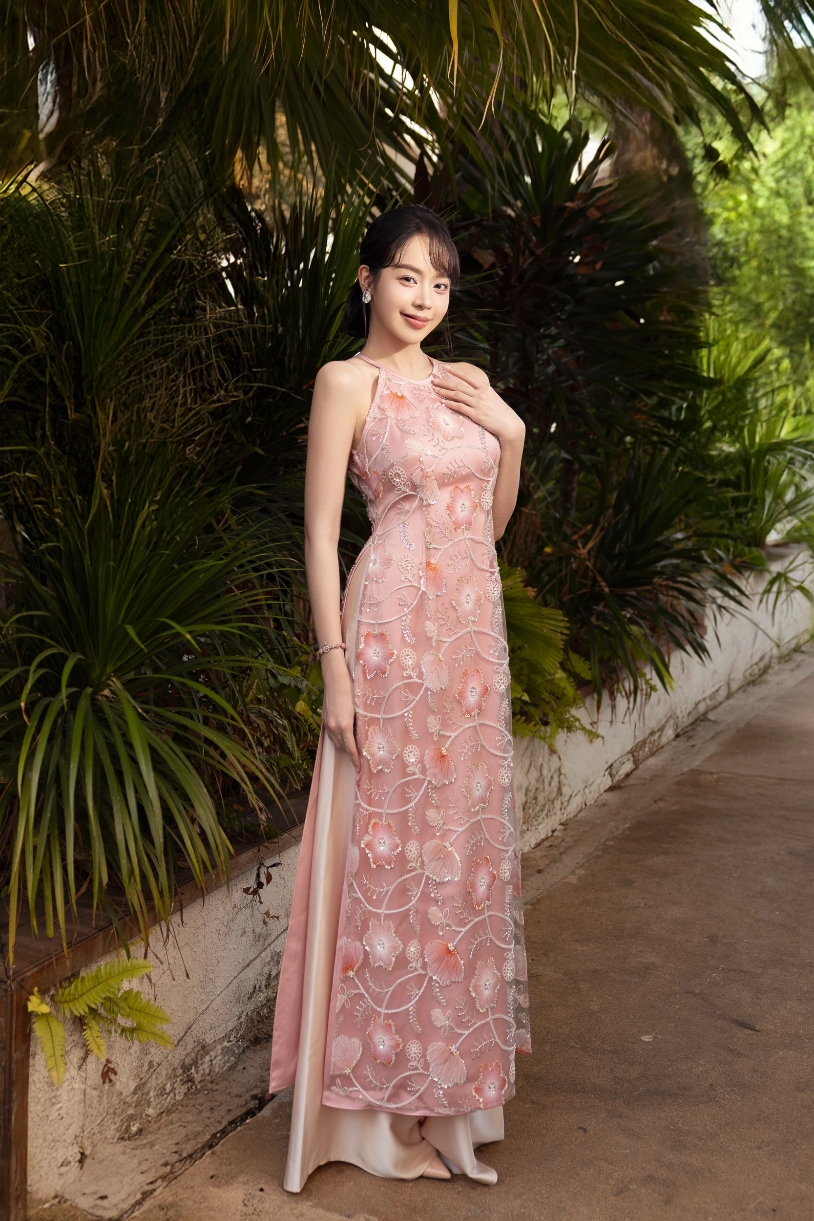 Chiếc áo dài hồng phấn với lớp voan thêu hoa nổi mang đến vẻ đẹp mong manh, lãng mạn như một nàng thơ cho hoa hậu Thanh Thủy. Thiết kế cổ yếm cách điệu phù hợp với những cô nàng gen Z trẻ trung, hiện đại.