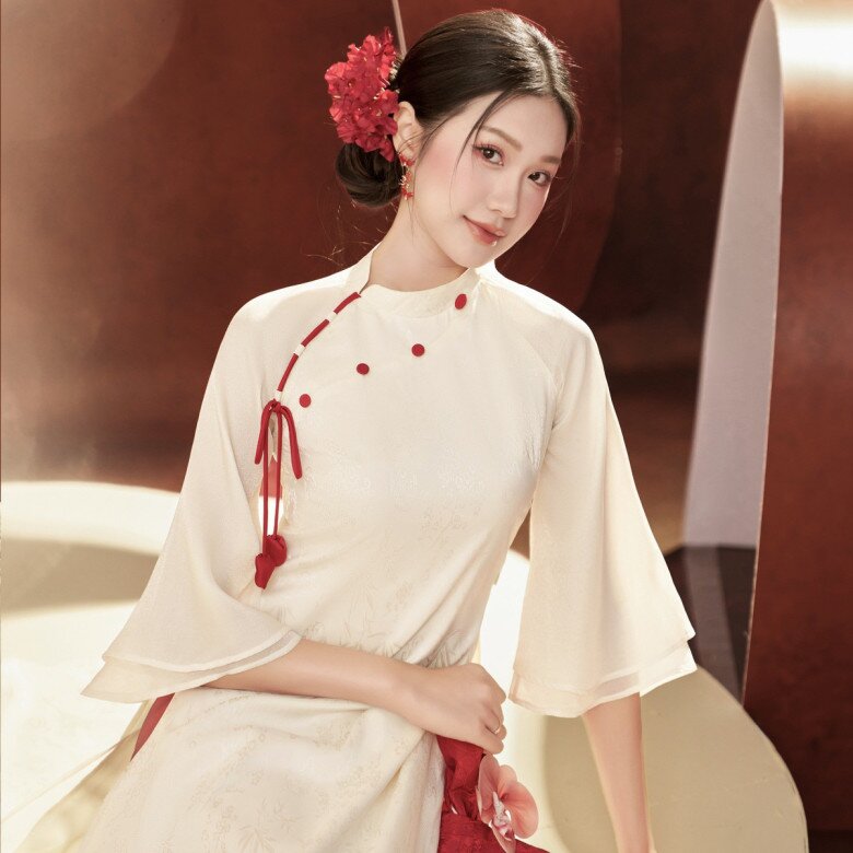 Doãn Hải My đẹp dịu dàng với áo dài lụa trắng ngà với hàng nút đỏ và chi tiết dây buộc cách điệu mang đến cảm giác cổ điển pha lẫn nét couture. Tay loe mềm mại tạo chuyển động uyển chuyển, trong khi phom dáng tối giản giúp tôn lên vẻ thanh lịch, chuẩn mực “nàng thơ” cho phái đẹp.