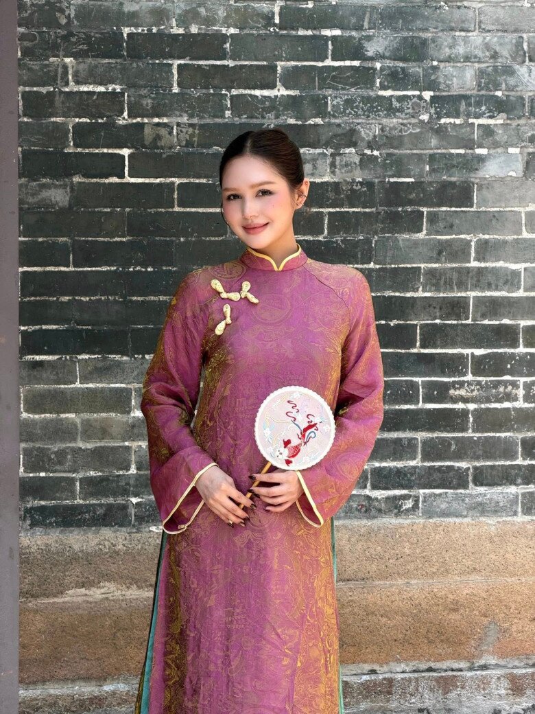 Hotgirl Xoài Non trông đẹp mặn mà, quý phái với chiếc áo dài gấm màu tím mận cùng họa tiết dệt chìm và đường viền vàng kim mang đậm tinh thần truyền thống. Phom dáng cổ điển, tay dài, kết hợp phụ kiện quạt tròn thêu tay giúp người mặc như bước ra từ một thước phim xưa.