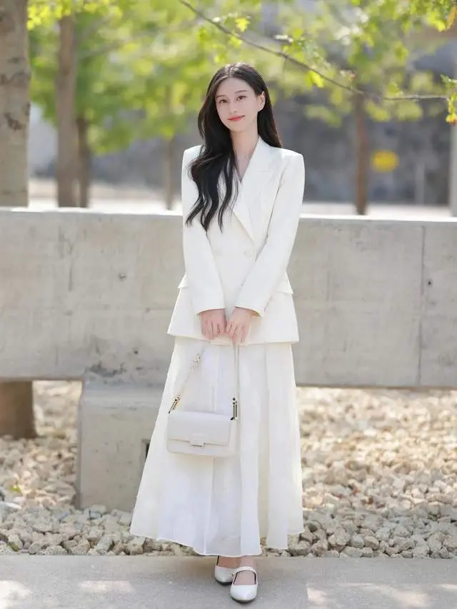 Bộ suit trắng ngà phối cùng chân váy dài đồng điệu tạo nên tổng thể “monochrome” nhẹ nhàng nhưng không hề nhạt nhòa để đi làm. Sắc trắng được xử lý khéo léo qua nhiều chất liệu khác nhau, giúp bộ trang phục có chiều sâu.