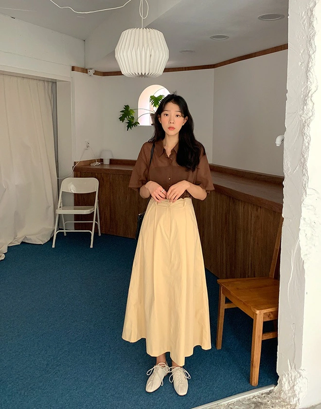 Chiếc sơ mi nâu trầm kết hợp cùng chân váy midi be sáng tạo nên bảng màu đất ấm áp, thanh lịch. Đôi giày trắng ngà là điểm kết mềm mại, giữ cho set đồ đủ trang nhã để đi làm nhưng vẫn phảng phất nét nghệ sĩ.