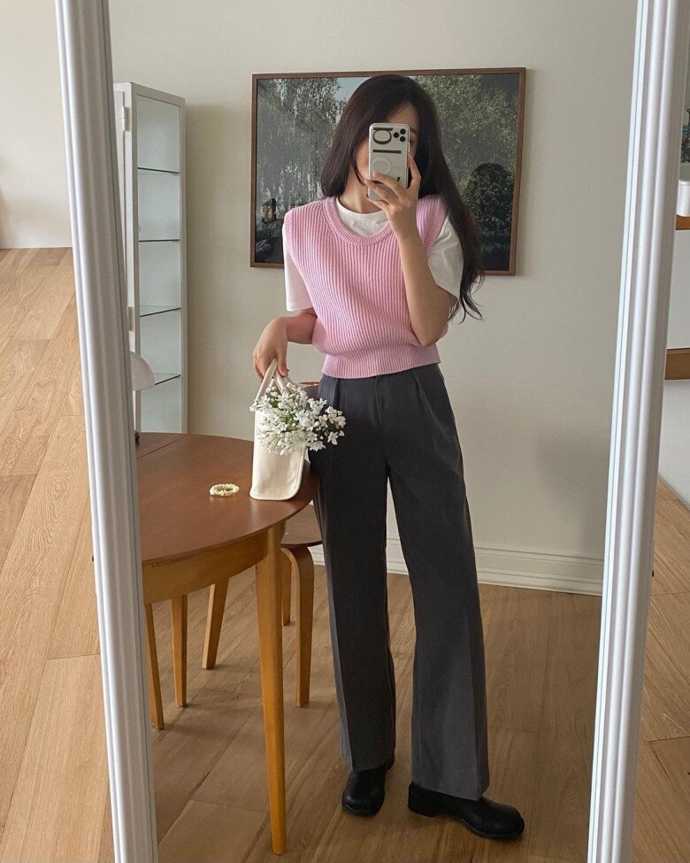 Quần xám đậm là màu chủ đạo, mang lại cảm giác tối giản và hiện đại. Áo gile hồng pastel tạo điểm nhấn trẻ trung, trong khi áo trắng đóng vai trò trung hòa bảng màu.