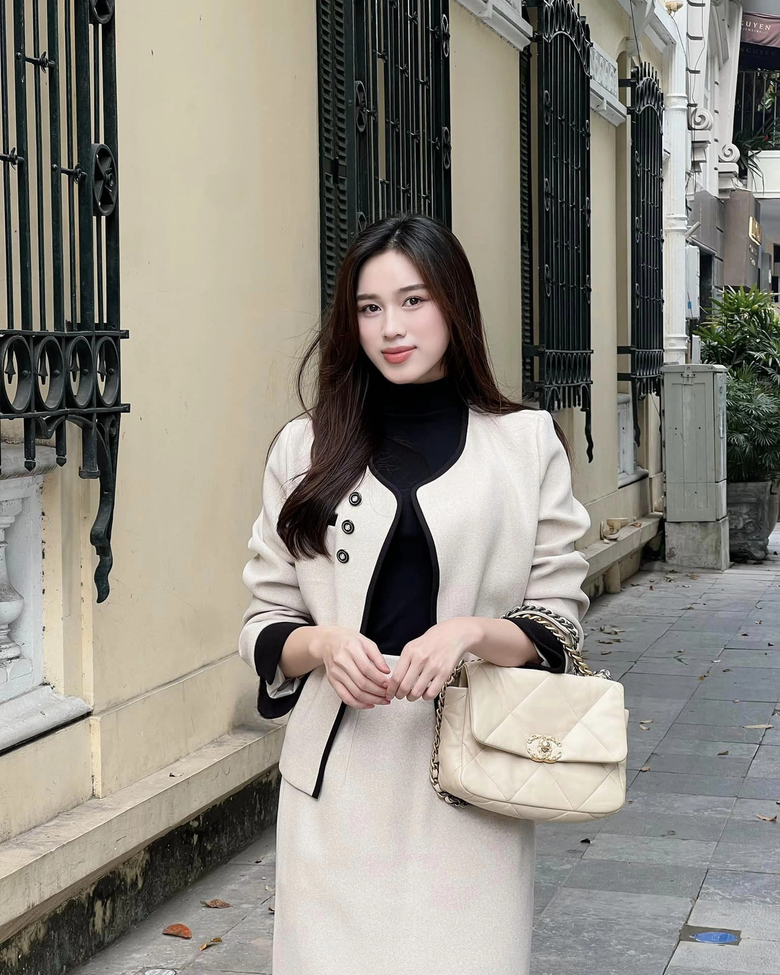 Vẫn áp dụng công thức phối màu đen trắng cơ bản, song hoa hậu Đỗ Hà thay áo khoác blazer bằng áo khoác tweed tông be phối cùng chân váy đồng bộ và áo cổ lọ đen bên trong tạo nên diện mạo chỉn chu, trang nhã cho môi trường công sở cao cấp