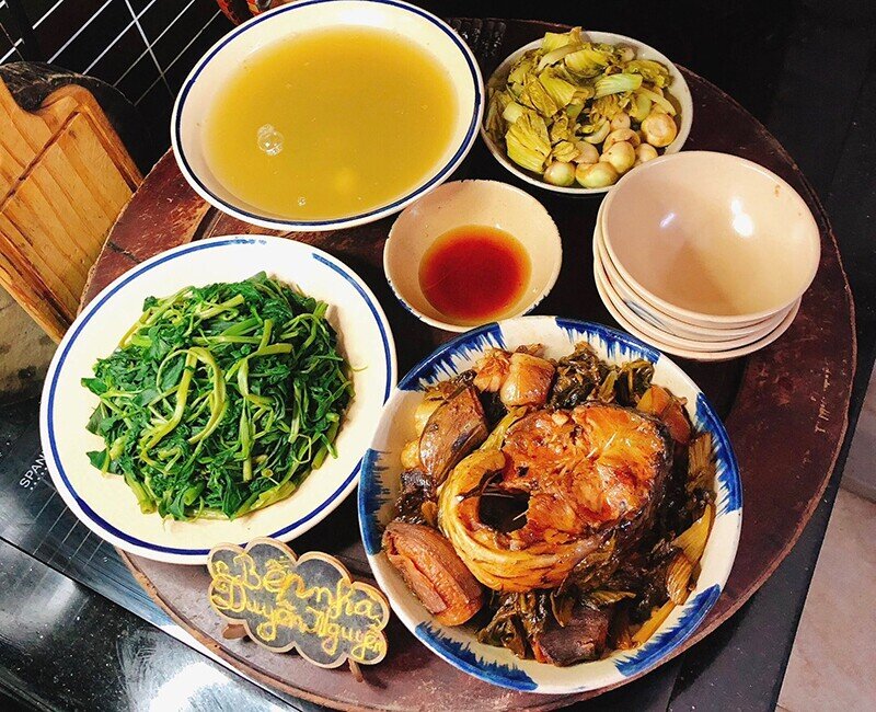 Mâm cơm này gồm các món: - Cá trắm đen kho ba chỉ và chuối xanh - Rau muống luộc - Canh rau muống luộc dầm sấu chua - Dưa cà muối.