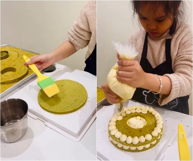 Để cốt bánh mềm và ẩm hơn, bé Gà dùng cọ quét một lớp nước đường lên bề mặt bánh trước khi bắt đầu phủ kem. Sau đó, cô bé tập trung cao độ để bắt từng hạt kem tròn đều tăm tắp lên lớp bánh đầu tiên.