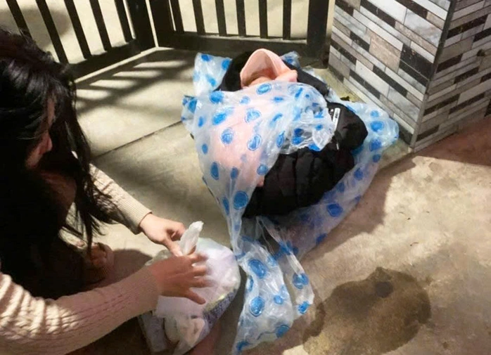 Bé trai được quấn trong áo ấm, kèm theo quần áo đặt trong một túi ni-lông