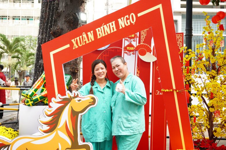 Chị Chọn (trái) và bệnh nhân nằm cùng phòng bệnh đã đón nhận không khí Xuân tại đường hoa. Chị Chọn tâm sự ở đây các bệnh nhân xem nhau như người nhà, luôn giúp đỡ nhau, động viên để vượt qua nỗi đau của kim tiêm, bệnh tật.