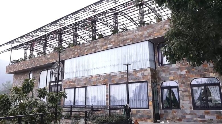 Ngoại thất căn nhà được ốp đá tự nhiên đa sắc với kiến trúc hiện đại, bao quanh là khuôn viên xanh mướt và hệ mái che phía trên sân thượng.