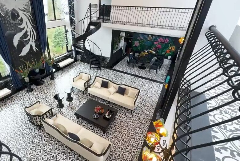 Góc nhìn từ trên cao xuống đại sảnh cho thấy sự bề thế của căn nhà với bộ sofa kem sang trọng và cầu thang xoắn ốc bằng thép đen đầy nghệ thuật.