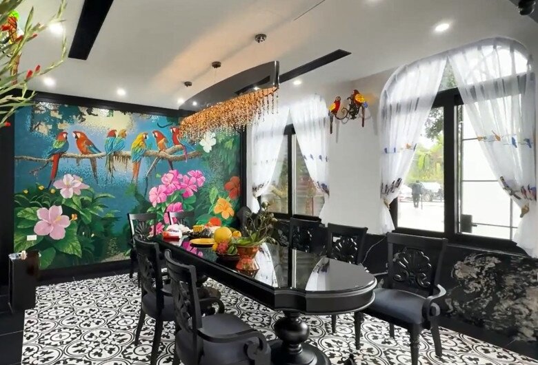 Phòng ăn gây ấn tượng mạnh bởi bức tranh tường chủ đề nhiệt đới rực rỡ và hệ đèn chùm pha lê hổ phách thả dài xuống bàn tiệc đen bóng sang trọng.