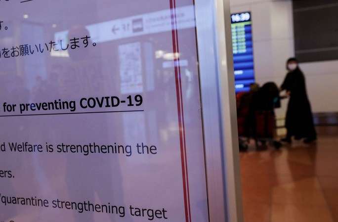 Một hành khách đằng sau bảng thông báo về các biện pháp Covid-19 tại sân bay Haneda, Tokyo - Ảnh: REUTERS