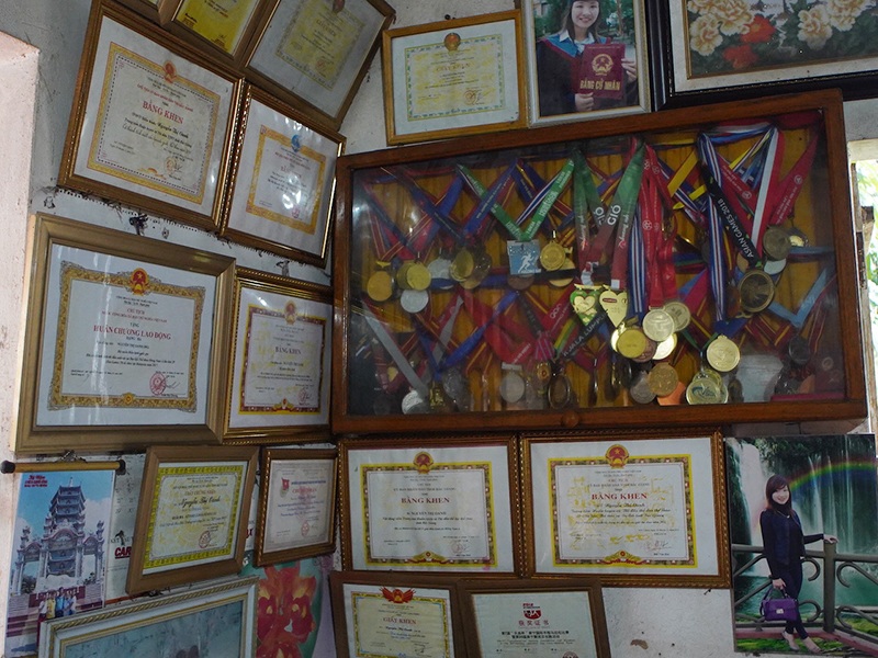 Trên tường ngôi nhà 3 gian cấp 4 lợp ngói được xây từ năm 2000, thứ khiến nhiều người khi vào nhà đều chú ý là rất nhiều bằng khen và cả một tủ kính treo tường đựng những huy chương của vận động viên điền kinh Nguyễn Thị Oanh đã đạt được
