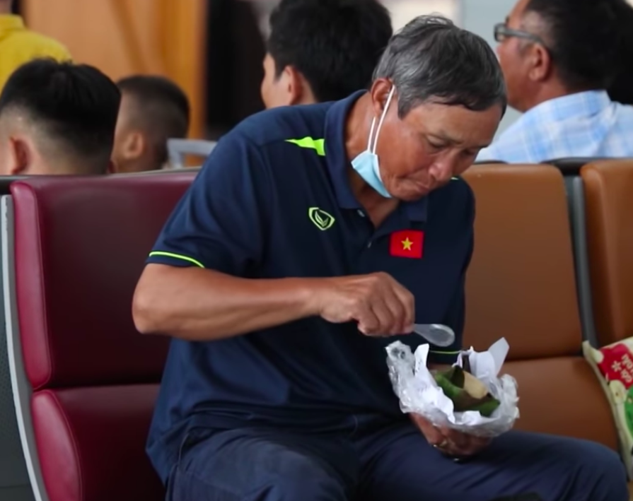 HLV Mai Đức giản dị ngồi ăn vội gói xôi trước giờ lên máy bay cùng đội tuyển bóng đá nữ Việt Nam sang nước ngoài tập huấn