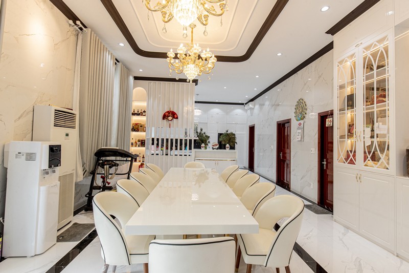 Phòng ăn với bàn dài và ghế bọc da trắng, tô điểm bằng đèn chùm lộng lẫy, bộ 12 ghế tựa đủ để cả nhà cùng quây quần ấm cúng.
