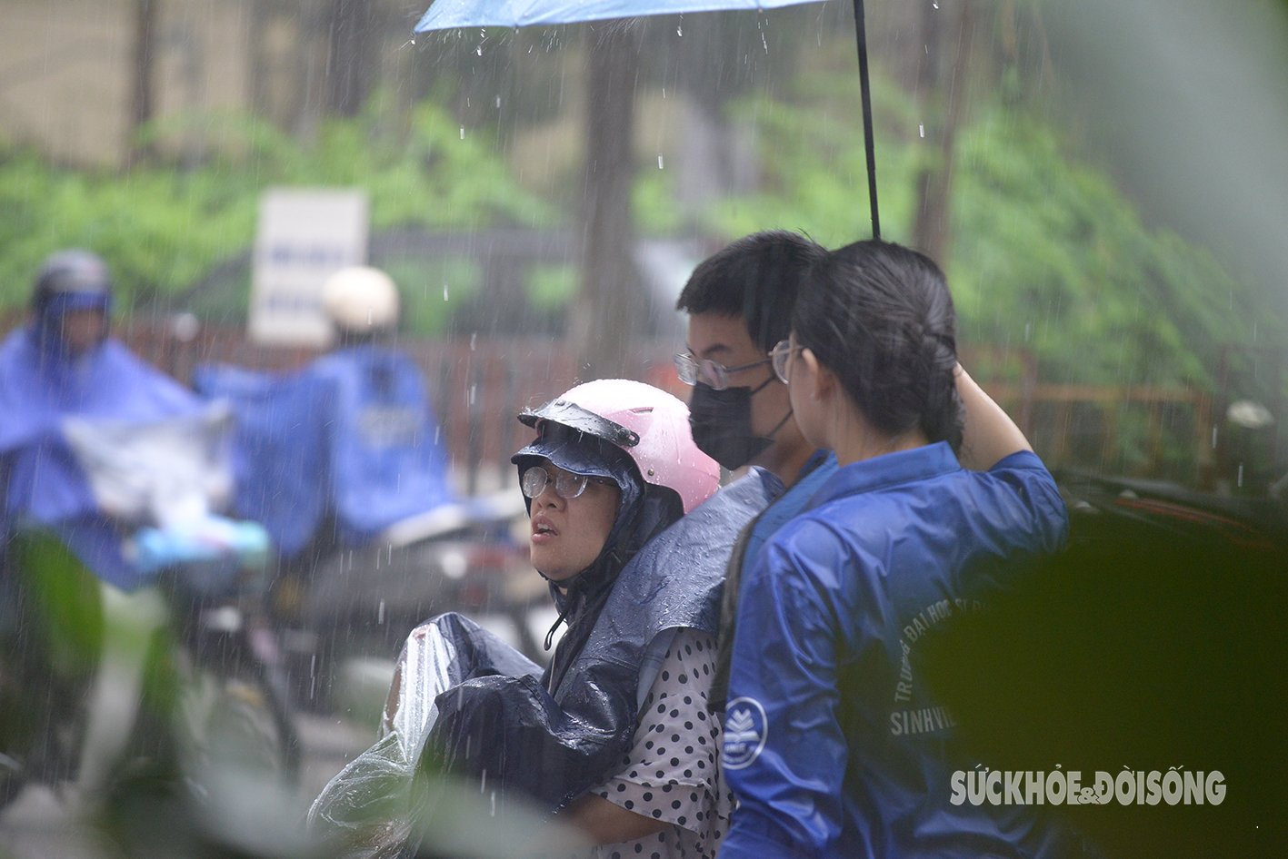 Tại điểm thi Trường THPT Chuyên Đại học Sư phạm, sinh viên tình nguyện đội mưa che ô hỗ trợ thí sinh vào phòng thi - một hình ảnh đẹp.