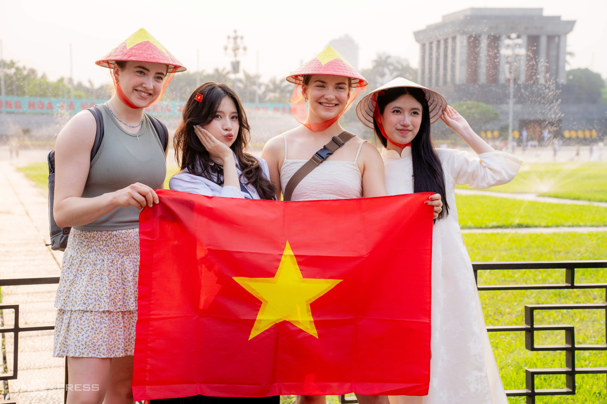 Du khách nước ngoài thích thú đội nón lá cầm Quốc kỳ chụp ảnh chung với người địa phương ở quảng trường Ba Đình.
