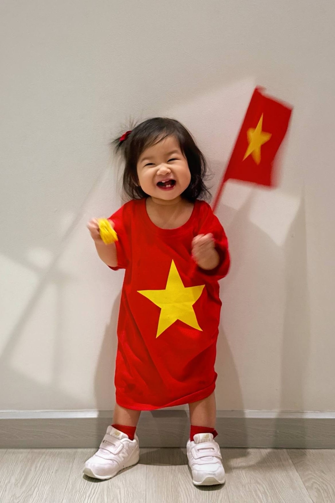 Bé Ayla nhà Á hậu Hoàng My bơi trong áo thun cờ đỏ sao vàng, cười tít mắt khi được mẹ cho tạo dáng với cờ Tổ quốc.