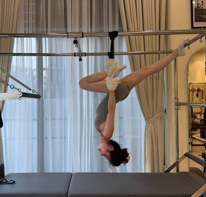 Chu Thanh Huyền thực hiện động tác treo ngược người, xoạc chân trên giường tập pilates.