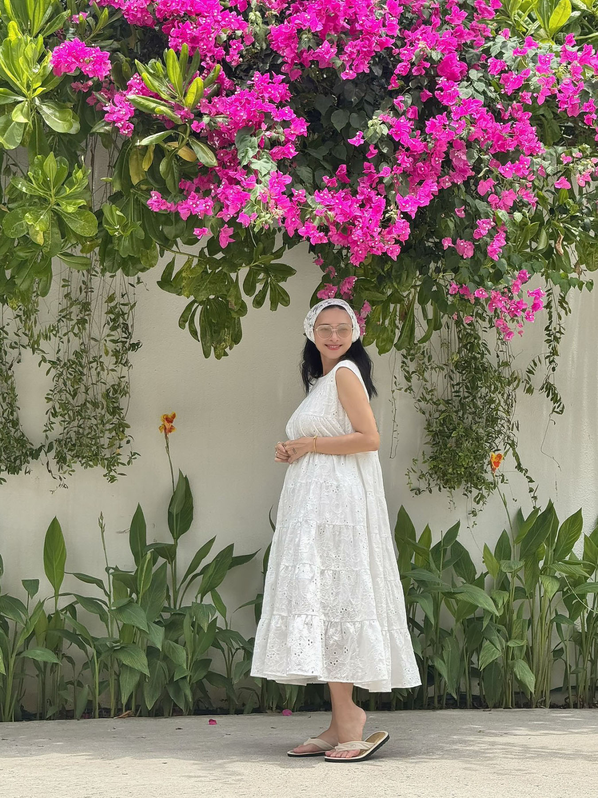 Người đẹp 46 tuổi chọn đầm trắng không tay phủ họa tiết chìm, nhấn nhá khăn buộc đầu đồng điệu trong kỳ nghỉ tại Nha Trang gần đây.