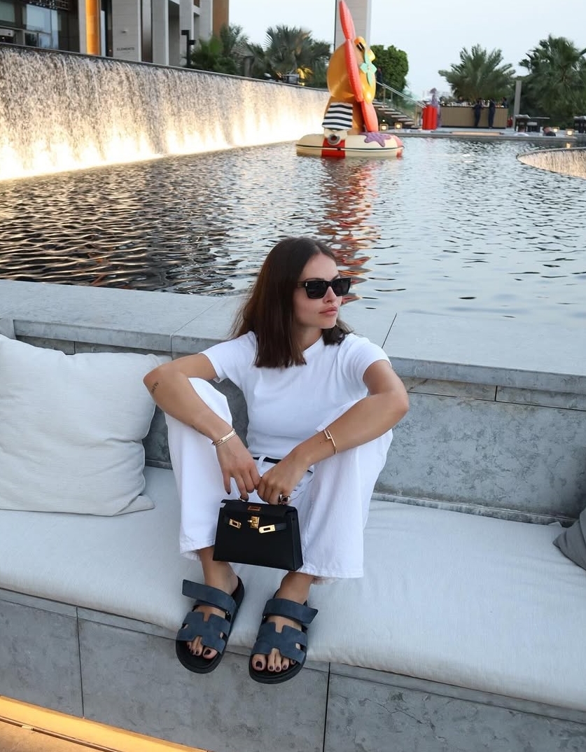 Áo phông và quần jeans trắng được tô điểm bằng phụ kiện tối màu gồm túi Kelly mini và sandals Hermes. Thylane chuộng túi và giày của hãng mốt này. Ngoài ra, cô còn có một số túi của Miu Miu và Chanel.