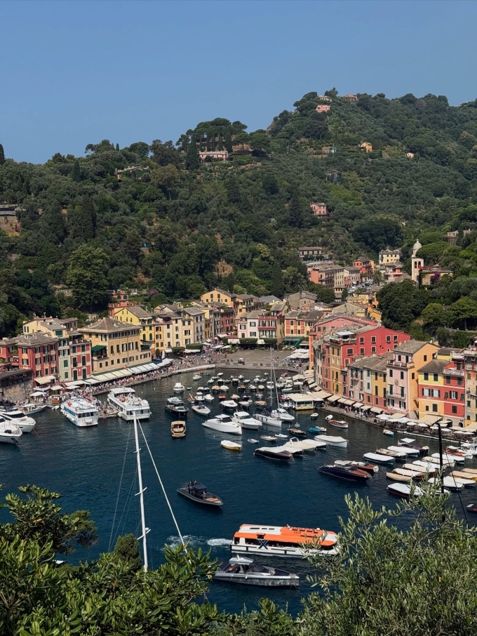 Portofino nổi bật với những ngôi nhà đầy màu sắc rực rỡ xếp tầng lên nhau dọc theo sườn đồi, ôm lấy bến cảng nhỏ xinh. Những tòa nhà mang gam màu pastel ấm áp như hồng đào, vàng chanh, xanh lam nhạt, bao quanh là những ngọn đồi xanh mướt được bao phủ bởi cây cối rậm rạp.