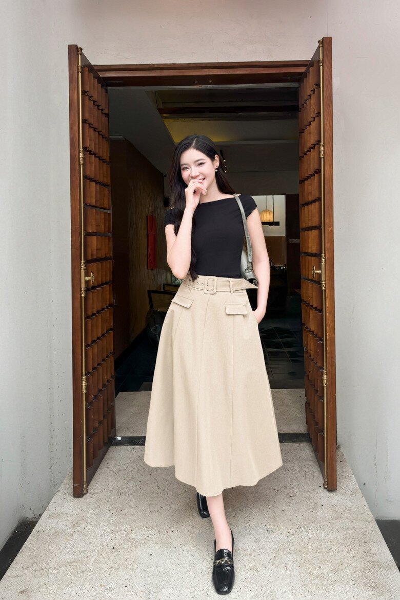 Áo ôm đen cổ thuyền kết hợp chân váy chữ A màu beige cùng đai bản lớn giúp định hình vòng eo, tạo cảm giác chân dài hơn.