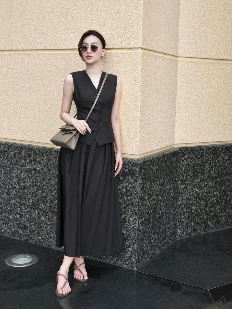 Tông đen toàn tập mang đến vẻ hiện đại, mạnh mẽ nhưng vẫn mềm mại nhờ chân váy midi xếp ly phối cùng áo gile ôm vừa vặn tôn dáng.