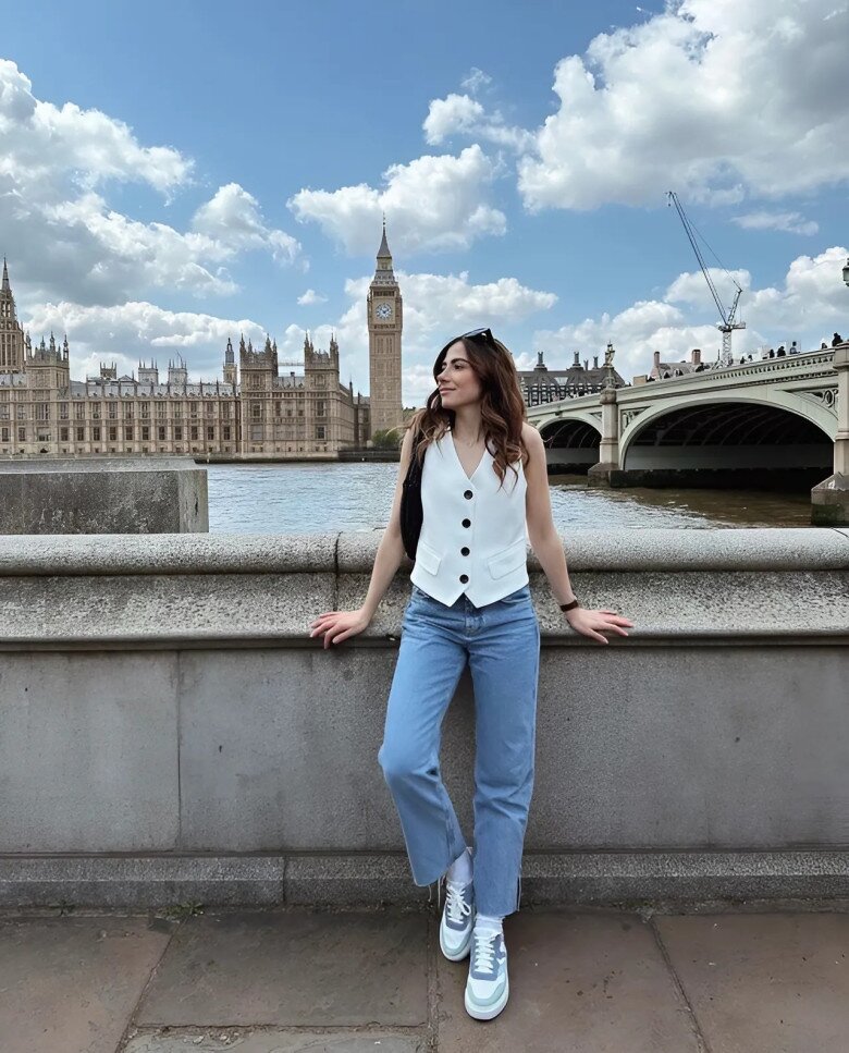 Áo gile trắng dáng cổ vest kết hợp cùng quần jeans ống đứng và sneaker, mang đến vẻ ngoài trẻ trung, hiện đại, đậm chất du lịch đường phố London.