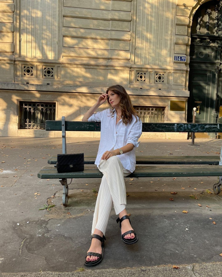 Set đồ tối giản đầy thanh lịch: sơ mi linen oversized trắng, quần lụa dập ly cùng sandal đế bệt cá tính. Phụ kiện Chanel cổ điển và đồng hồ mảnh mai tạo điểm nhấn cho vẻ đẹp nhẹ nhàng mà tinh tế.
